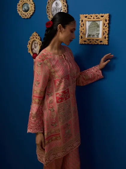 A profile shot that feels like a candid moment. The model interacting with the picture frames adds a touch of storytelling to this fashion image, highlighting the intricate print of the pink kurta.