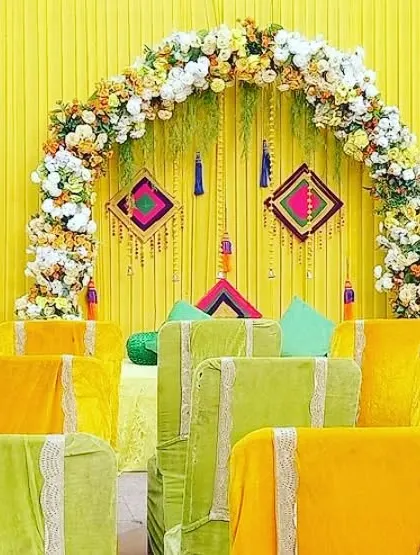 A beautiful floral arch against a bright yellow backdrop, with covered chairs arranged for guests. This setup is ideal for a formal Mehendi or Haldi lunch.