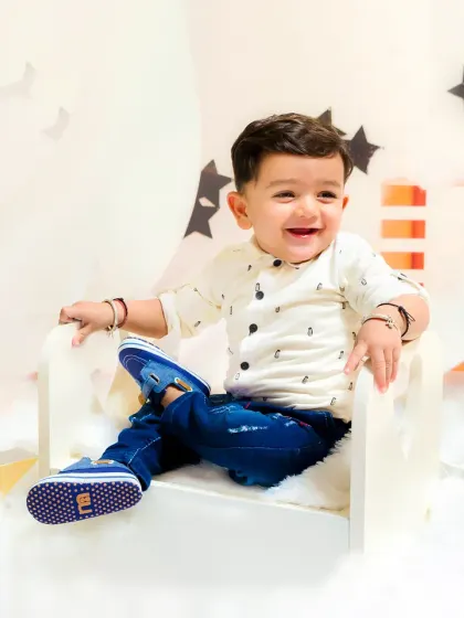 A baby boy flashes a huge, happy smile from his miniature armchair in a star-themed setup. His joy is absolutely infectious.