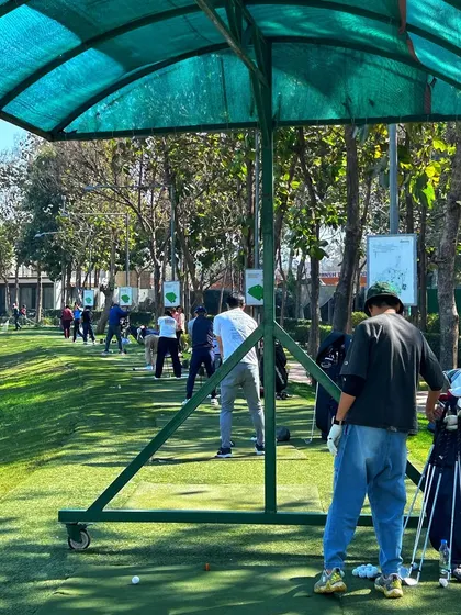A golfer watches his shot from a covered bay on a bright, sunny day.