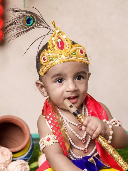 This little Krishna is looking right at the camera with a sweet smile. The details of his costume, from the pearl necklaces to the red sash, are beautifully captured.