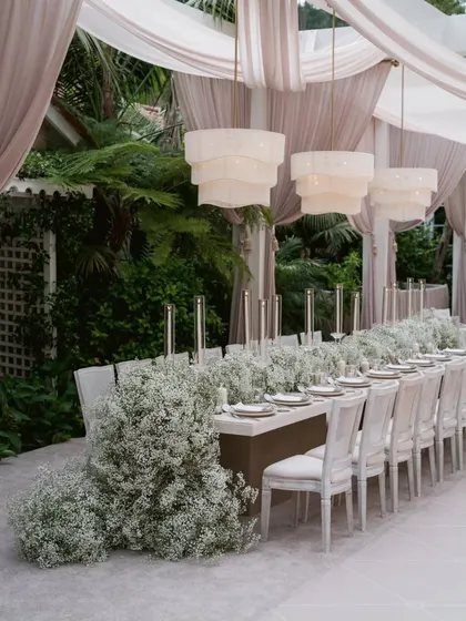 This is where elegance meets drama. I designed this immersive dining experience with a cascading runner of baby's breath flowers flowing down a long table, illuminated by modern tiered chandeliers and the soft glow of candlelight for a truly magical anniversary dinner.