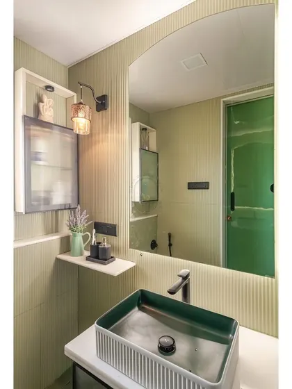 A closer look at the vanity area in the green bathroom. The rectangular vessel sink has a textured exterior that complements the fluted walls, and the arched mirror softens the clean lines of the space.