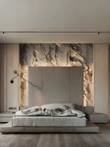 A luxurious master bedroom with a dramatic stone-finish accent wall behind the bed. The combination of an upholstered headboard, soft backlighting, and modern sconces creates a sophisticated and relaxing ambiance.