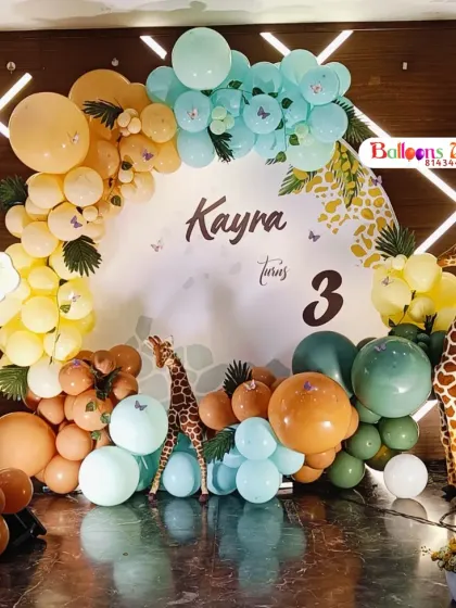 A detailed look at a safari-themed birthday for Kayra's third birthday. This setup includes a custom circular backdrop, a colorful balloon arch, and a variety of animal figures like a lion, giraffe, and zebra.