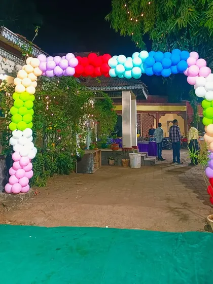 An outdoor entrance decorated with a vibrant, multi-colored balloon arch. This is a great way to welcome guests to a party held in a garden or farmhouse, making the entrance clearly visible and festive.