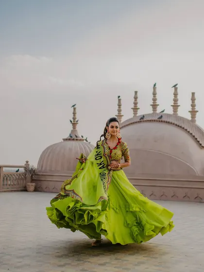 A beautiful shot of the bride in a vibrant green lehenga, twirling on a rooftop in Jaipur during her Mehendi ceremony. The movement and color are captivating.