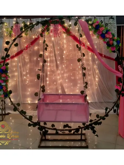 An elegant cradle ceremony setup featuring a circular frame decorated with vines and flowers, with a sheer curtain and fairy lights creating a magical backdrop.