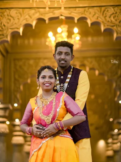 A happy portrait of a couple in colorful traditional attire. The warm lighting and ornate background make this a rich and festive photo.