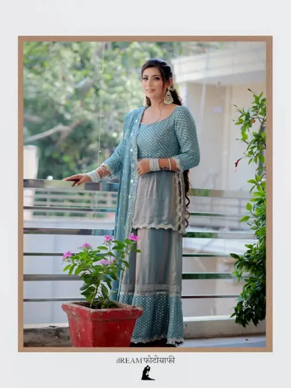 A full-length shot of Mannat on a balcony, her elegant blue outfit complemented by the greenery around her.