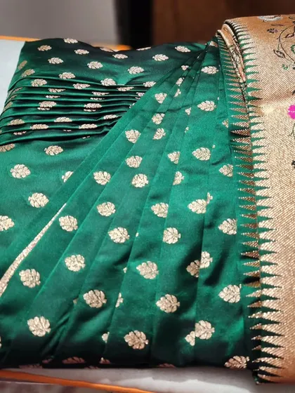 A close-up of the pre-pleated emerald green Banarasi saree for a Maharashtrian bride. The pleats are set and ready for box-folding, making it easy to store and transport before the event.