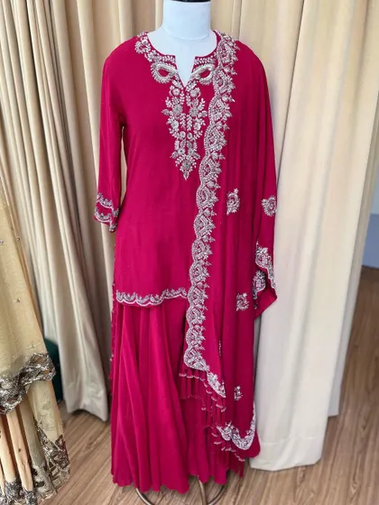 A studio shot of a vibrant pink Moonga silk kurta sharara set. The intricate silver embroidery on the neckline and dupatta makes this a standout piece for any festive occasion.