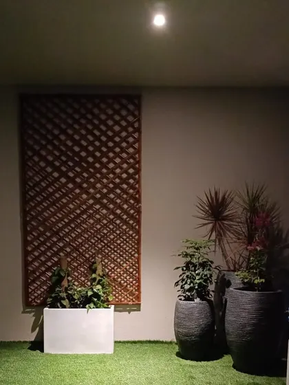 A minimalist night-time balcony setup. Artificial turf, a wooden trellis, and a few carefully placed planters with uplighting create a clean, stylish, and low-maintenance green area.