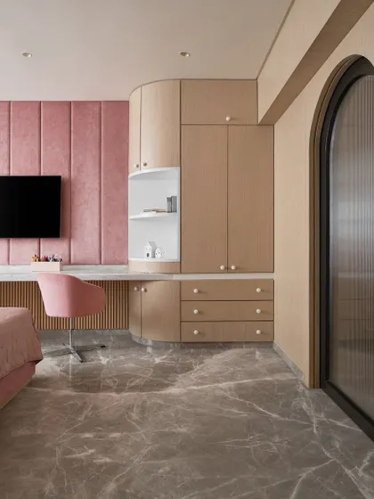 A view of the custom curved wardrobe and study unit in the kid's bedroom. The design maximizes storage and provides a functional workspace while maintaining a soft, inviting aesthetic.