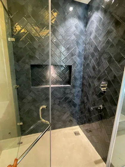 A view into the shower cubicle, showing the rich, dark chevron tiles that cover the walls. A built-in niche provides convenient storage for shower essentials.