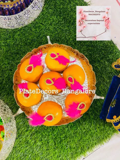 A golden plate of oranges decorated with bright pink feathers and kundan stones, offering a playful and vibrant look.