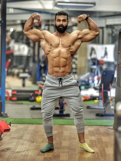 Another front double bicep pose, this time in pants, showing that a well-built physique commands attention even when not in competition trunks.