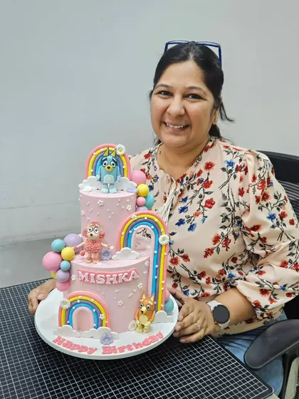Posing proudly with the colorful, two-tier Bluey-themed cake.