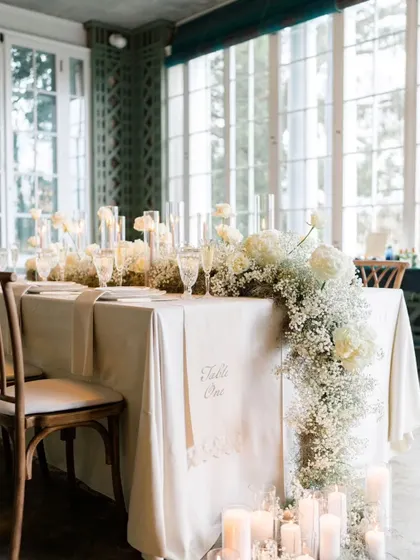 A beautifully styled table with a cascading floral arrangement of baby's breath. The clean white linen and pillar candles create a look of timeless elegance.