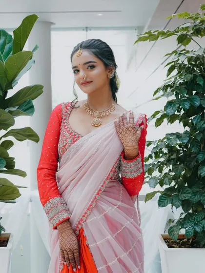 A modern take on traditional wear. This custom lehenga-saree features a heavily embroidered red blouse with full sleeves, paired with a light pink and orange draped saree.