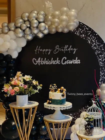 A full view of the classy black, white, and silver decor for a 30th birthday. The circular backdrop, balloon garland, and elegant dessert stands come together for a polished and modern look.