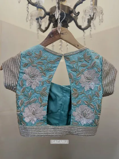 A sparkly floral embroidered blouse in a combination of light gold and silver detailing on a powder blue base, with a stylish back cutout.