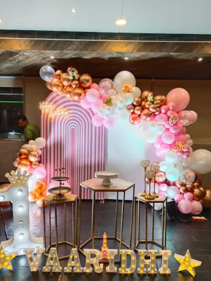 A beautiful and modern first birthday setup in shades of pink and rose gold. The arched backdrops and metallic balloons create a very trendy and stylish look.