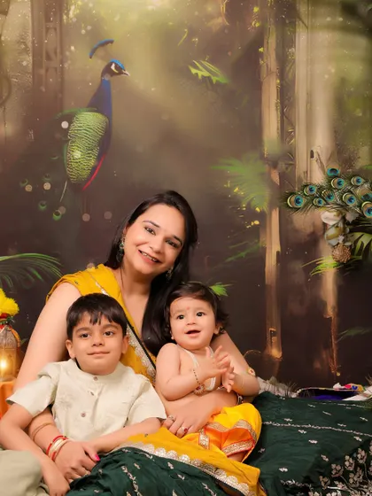 A beautiful family portrait taken during a Janmashtami session. The mother holds her two children, one a toddler and the other a baby dressed as Krishna, against our signature peacock backdrop.