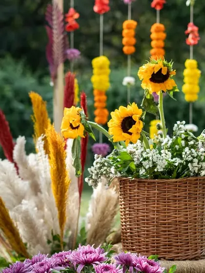 A beautiful arrangement of sunflowers and pampas grass in a wicker basket, with a backdrop of hanging marigold strings for a rustic Haldi.