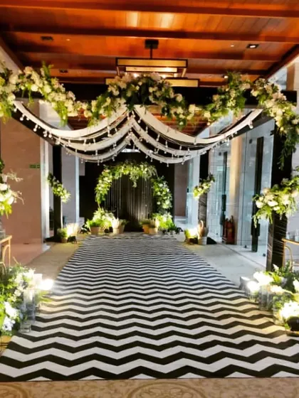 A modern and chic entrance for an engagement party. The black and white chevron carpet runner and the white floral arrangements create a sophisticated and stylish look.