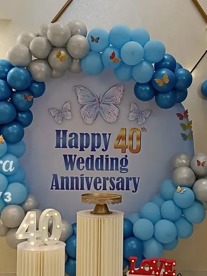 Celebrating a 40th wedding anniversary in style. This beautiful setup includes a circular backdrop, a blue and silver balloon arch with butterfly details, and light-up marquee numbers.