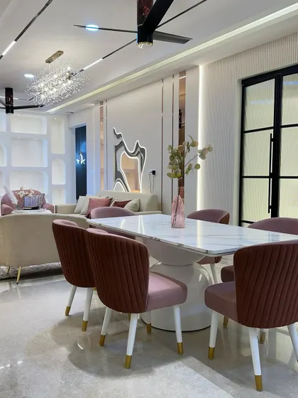 This glamorous dining room features plush pink velvet chairs and a modern white marble table. The statement chandelier and designer fan add a touch of luxury to the space.