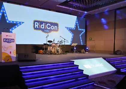 Another view of the 'RidiCon' stage, showing the illuminated steps and branded lectern. The entire setup is designed to be immersive and reinforce the event's brand identity.