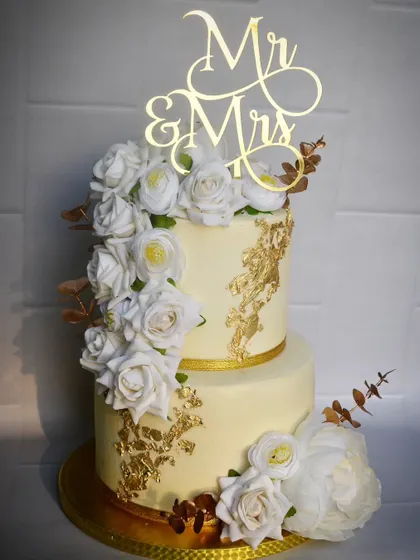 A classic and elegant two-tier wedding cake in ivory and gold. The cascade of white sugar roses and gold leaf accents creates a timeless and sophisticated look.