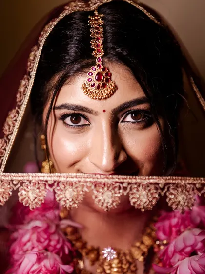 A playful close-up of the bride peeking through her veil. This shot highlights her beautiful eye makeup and radiant smile.