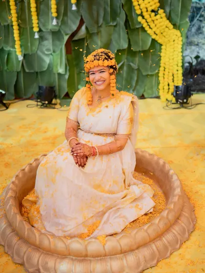 A serene portrait of the bride after her Haldi ceremony, covered in yellow petals against a backdrop of marigolds.