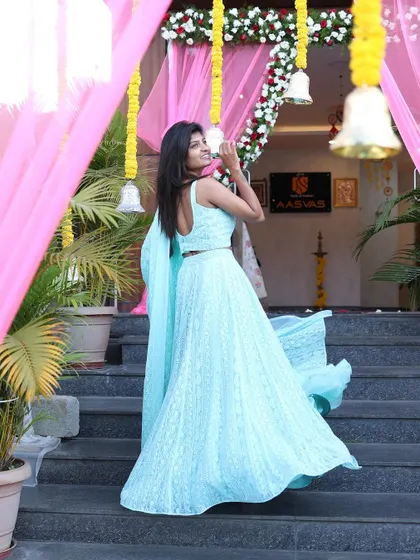 A beautiful shot of a model in a light blue lehenga, taken at an event entrance. The flowing fabric and joyful pose make it a perfect shot for event or celebration wear.