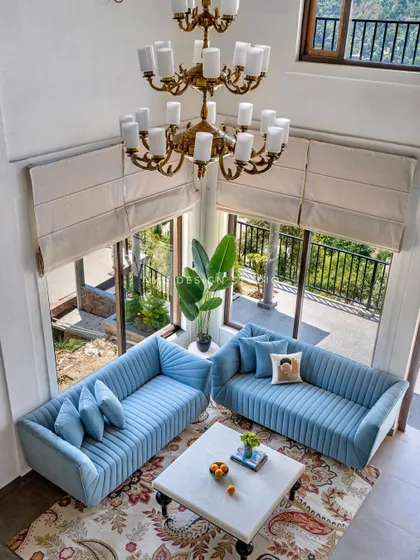 An aerial view of the double-height living room in our Mukteshwar project. The two custom-made, channel-tufted blue sofas anchor the space under a grand chandelier, creating an atmosphere of pure luxury.