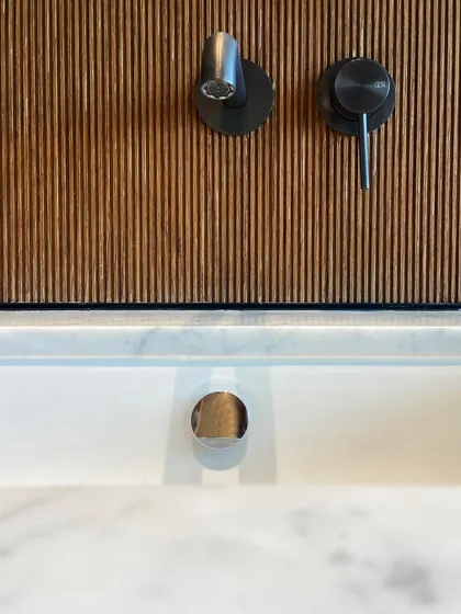In this bathroom detail, the cool, clean lines of the marble sink and countertop are contrasted with the warmth of a fluted wood backsplash. The modern black fixtures from Gessi provide a sharp, graphic accent.