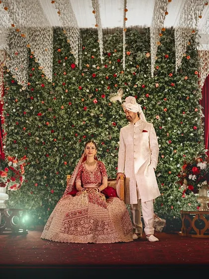 A grand stage, a wall of flowers, and a couple looking like royalty. This is a perfect example of a classic wedding stage portrait.