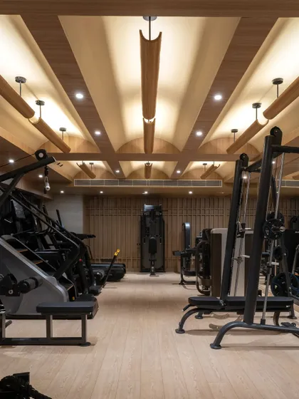 The gym at Be Well, where the architectural language of the rest of the center continues. The coffered wooden ceiling with integrated lighting creates a warm, uplifting atmosphere for exercise.