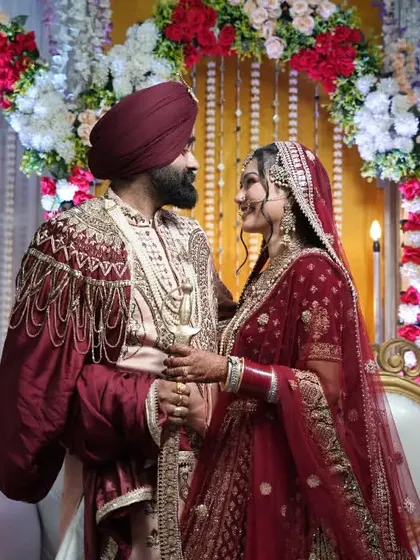 A regal portrait of a Sikh couple on their wedding stage, dressed in rich maroon and gold attire.