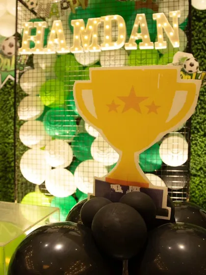 A close-up of a trophy prop against the green balloon and mesh backdrop, adding to the championship feel of the party.
