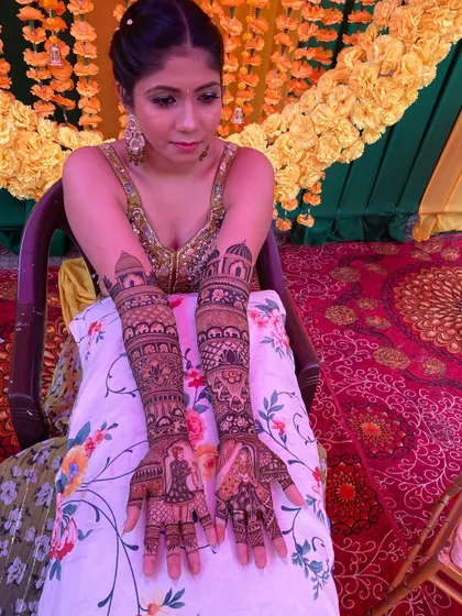 A beautiful bride posing with her full bridal mehandi. The design features portraits on the palms and architectural domes on the arms.
