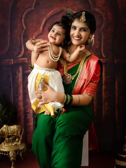 A heartwarming portrait of a smiling baby Krishna held by his mother. The pearl necklaces and traditional dhoti complete the look.