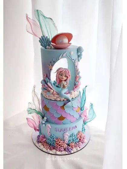The finest mermaid cake we've created. This stunning, multi-tiered cake features a central cutout with a mermaid inside, intricate scale patterns, and delicate, translucent fins.