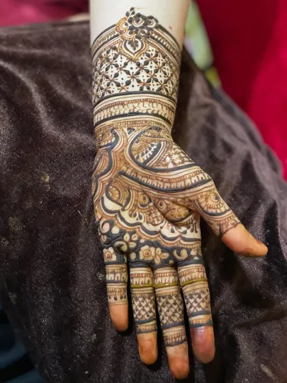 A close-up of a single hand with a heavy, intricate design. The pattern combines checks, swirls, and floral elements.
