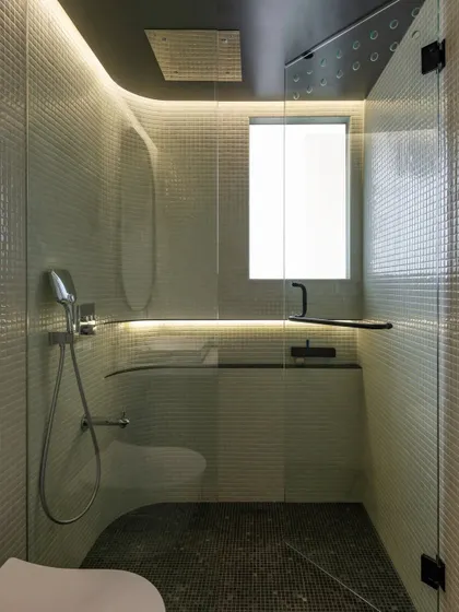 A bathroom featuring curved walls lined with white mosaic tiles and illuminated with soft, integrated backlighting.