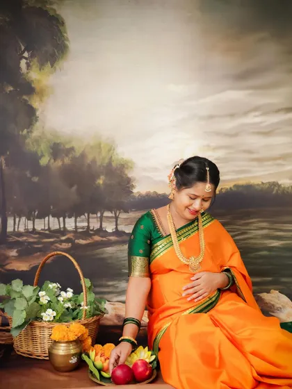 A traditional South Indian maternity portrait. The mom-to-be is dressed in a beautiful orange and green saree, surrounded by cultural elements.