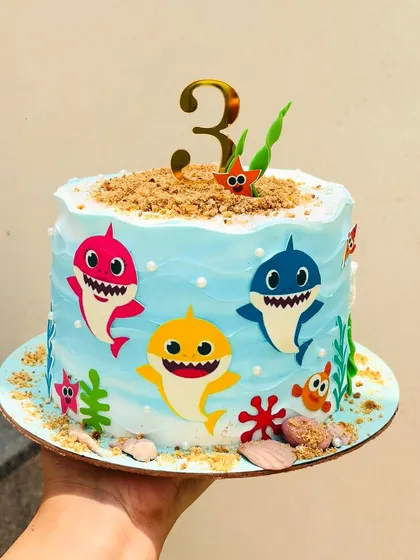 This Baby Shark cake is ready for a third birthday party. The design includes the whole shark family, edible sand, and little seaweed details for a complete ocean adventure.